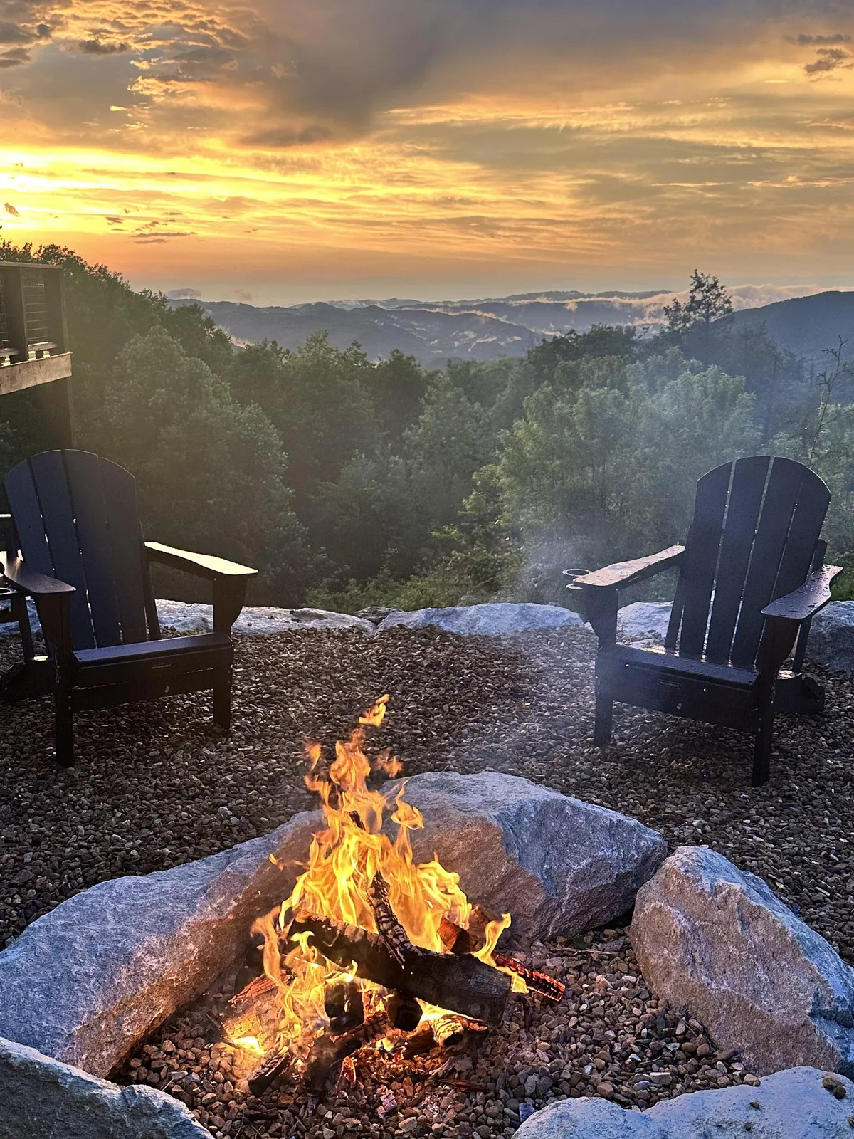 A cozy outdoor fire pit area with a circle of rock seating and lively flames, set before a stunning mountain view. The atmosphere is warm and inviting, perfect for family gatherings, storytelling, and admiring sunsets or starry skies.