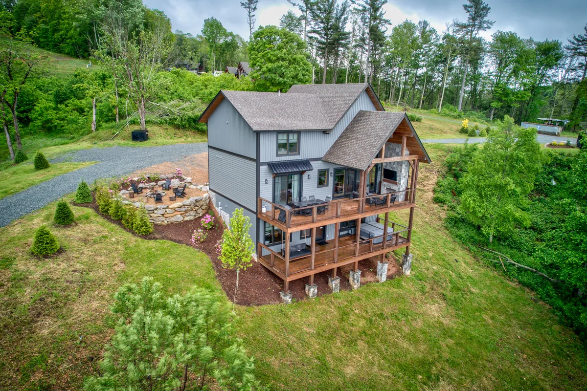 An inviting exterior image of the house, focusing on the deck and fire pit area surrounded by lush greenery. The expansive deck offers ample space for relaxation and sunset viewing, perfectly positioned to enjoy a glass of wine outdoors.