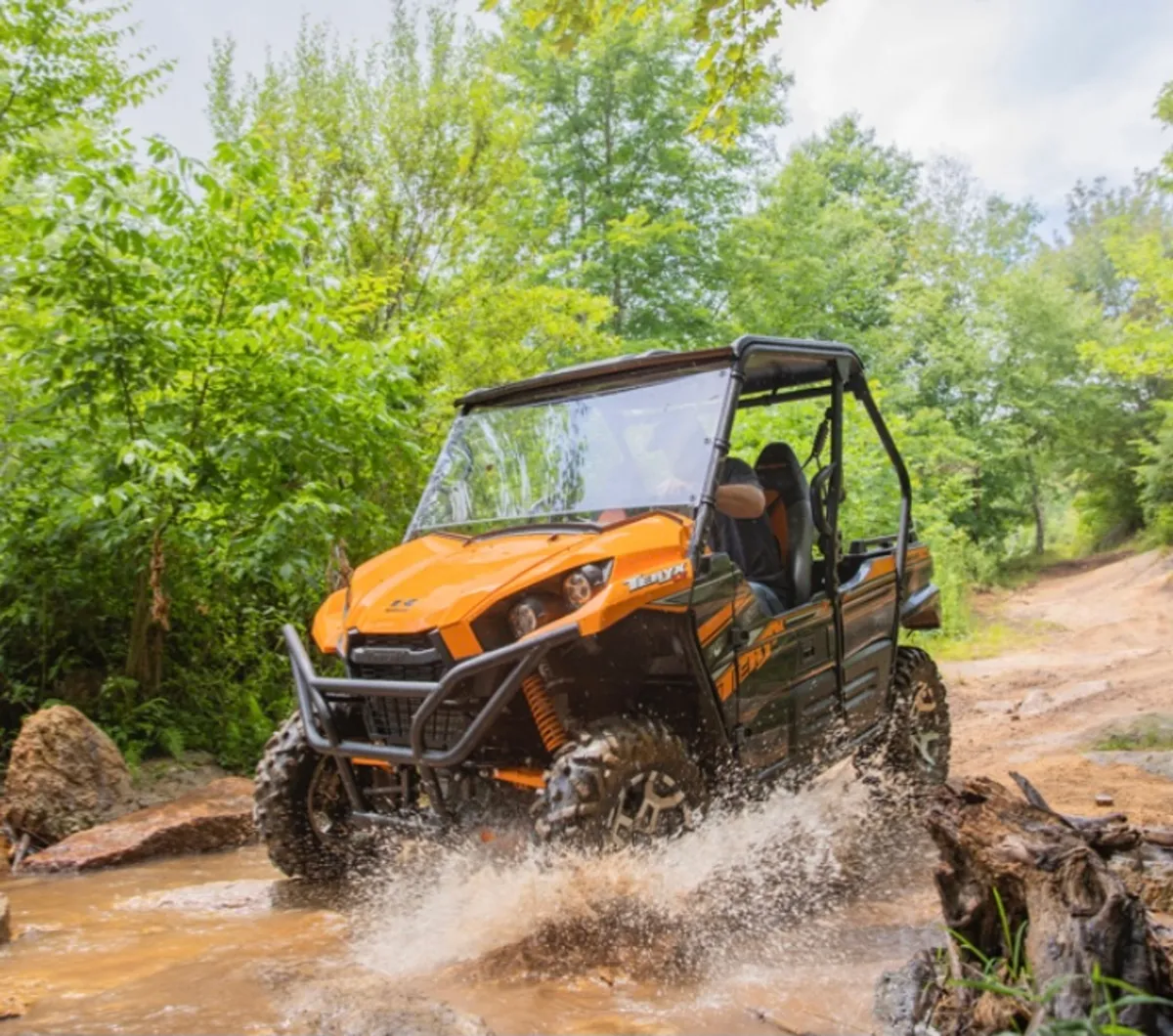 An action-packed scene featuring an ATV splashing through water, surrounded by lush greenery. The dynamic composition emphasizes off-roading and adventure in a natural setting.