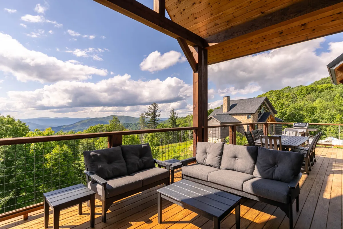 A tranquil deck scene with comfortable outdoor seating, wooden beams, and sweeping mountain views. The image radiates peace and a strong connection to the natural setting, suggesting opportunities for relaxation and reflection during a stay.