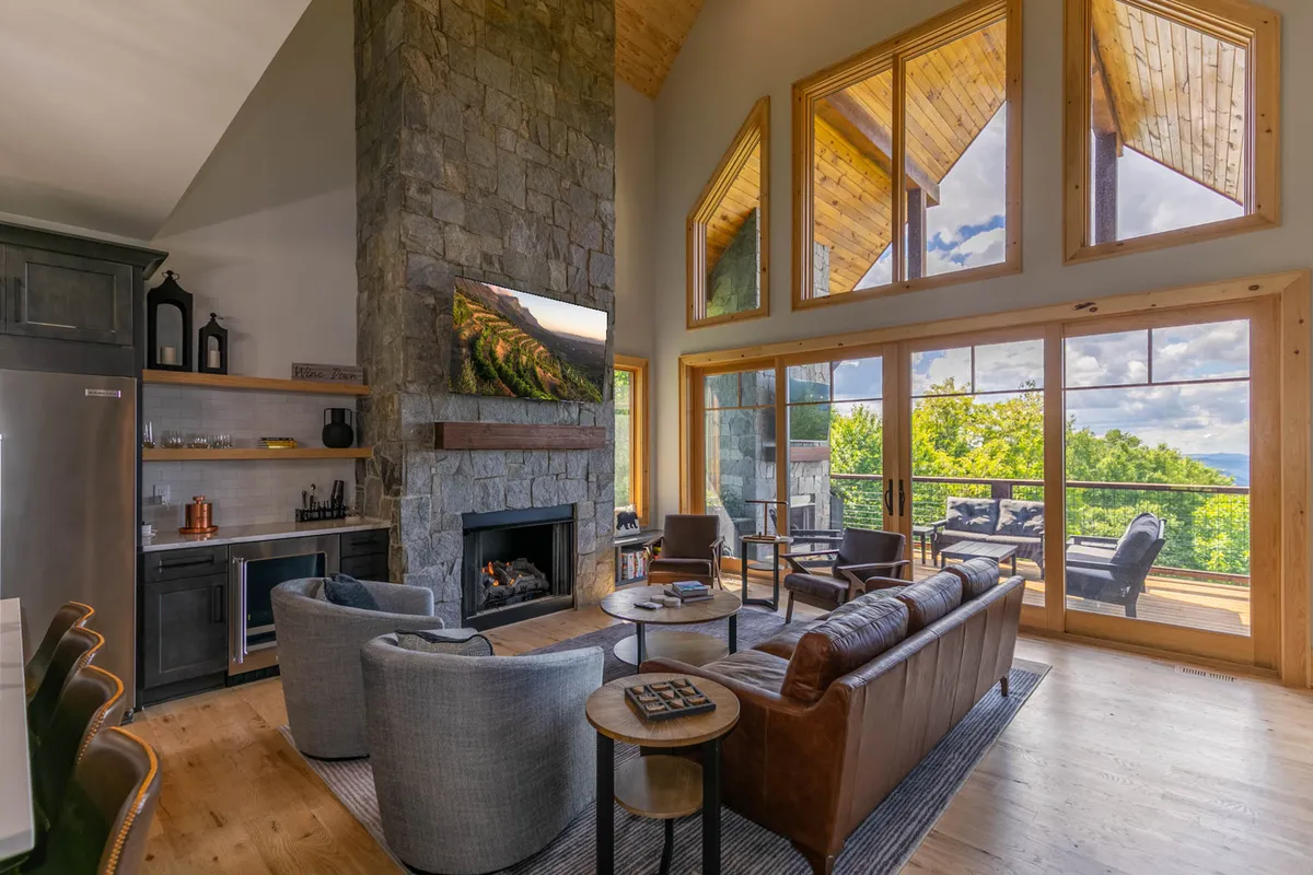 A welcoming great room featuring a large stone fireplace, floor-to-ceiling windows that flood the space with natural light, and a comfortable seating arrangement ideal for socializing or relaxing by the fire.