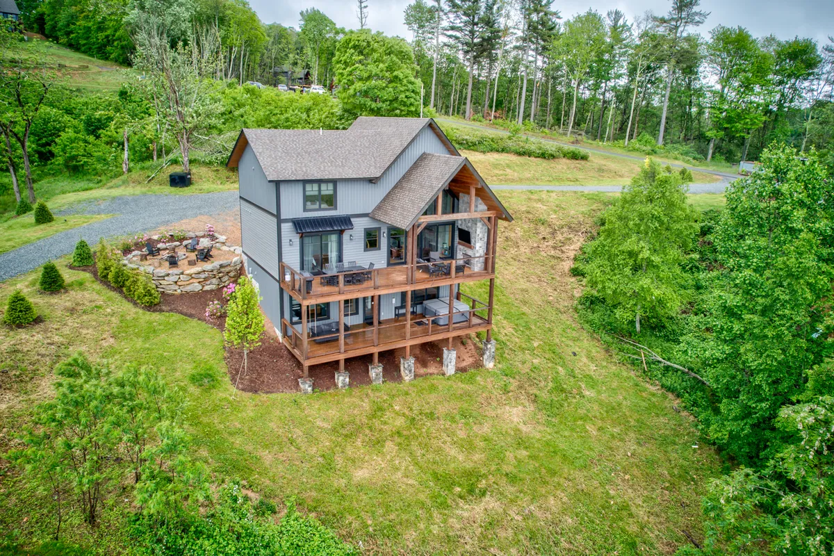A welcoming mountain home with a spacious deck and a well-arranged fire pit area, surrounded by natural greenery. The deck is set for outdoor gatherings, with plenty of space for groups to relax or share meals, and the fire pit is ready for cozy evenings under the stars.
