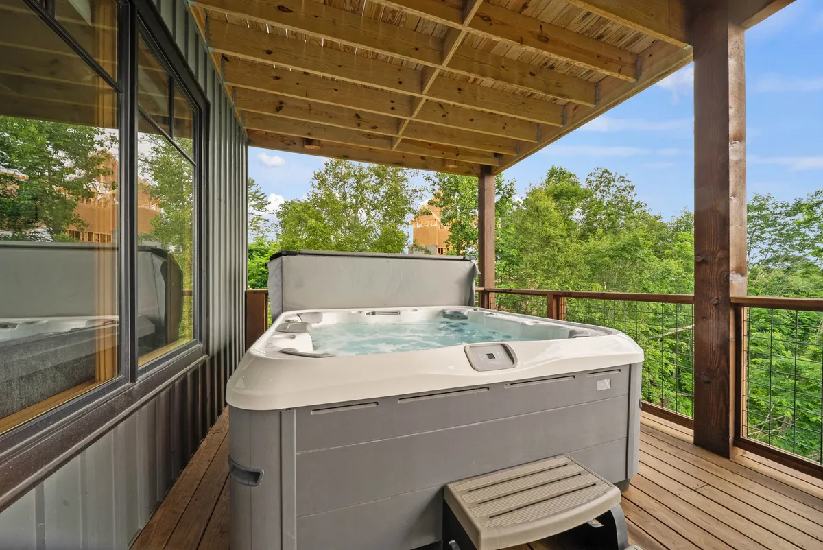 A serene wooden deck featuring a hot tub with surrounding greenery. The peaceful outdoor setup invites relaxation and socializing while immersed in nature.