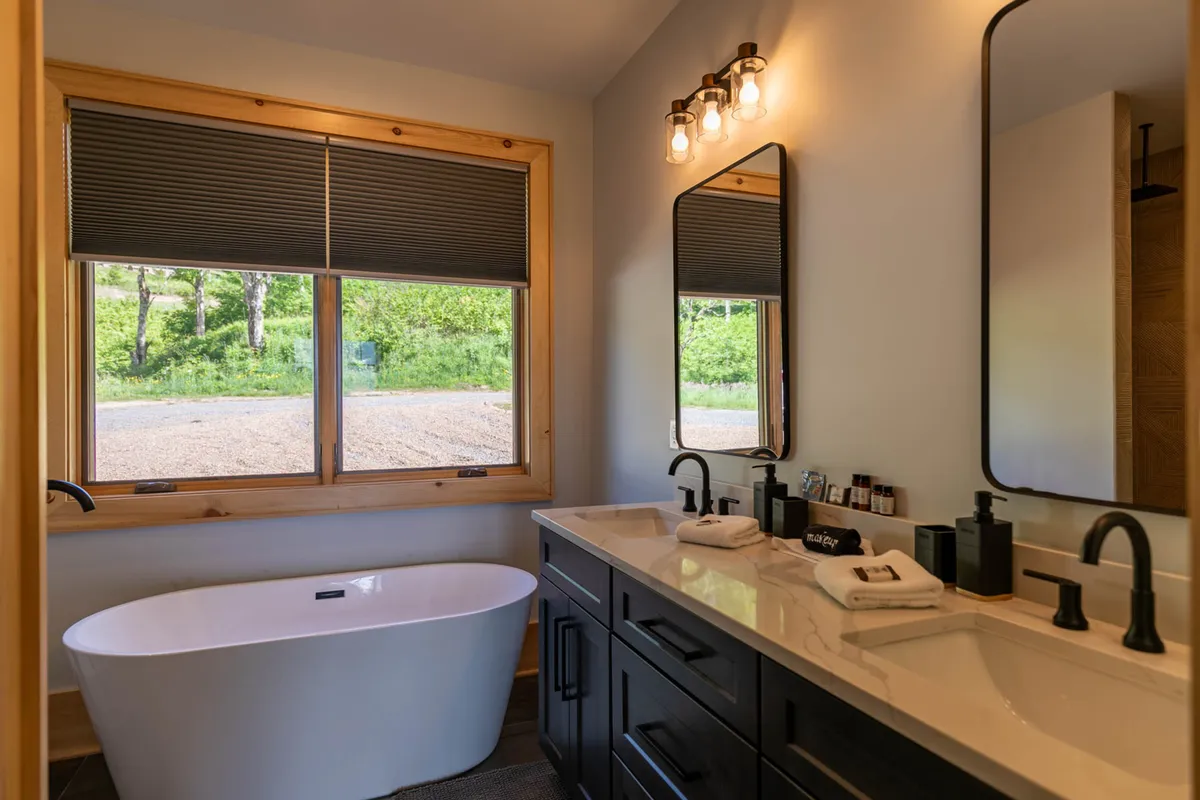 A spa-inspired bathroom featuring a freestanding soaking bathtub, a double-sink vanity, and a large window that fills the space with rejuvenating natural light. The clean lines and minimal design evoke a sense of luxury and tranquility.