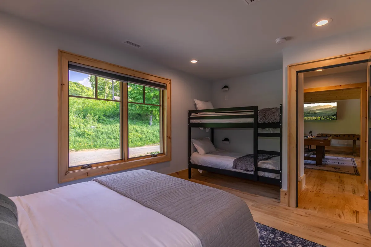 A cozy bunk room with a sturdy bunk bed, plush bedding, and a large window that streams in morning sunlight. The space feels inviting and playful, perfect for children or teens to unwind after a day of adventure.