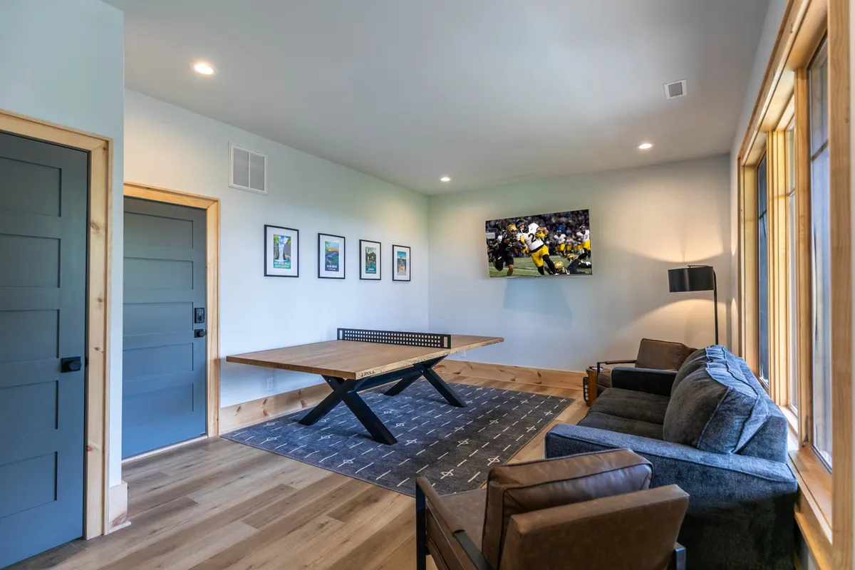 A comfortable lower-level room featuring a large table, sofa, television, and wall artwork. The set-up is perfect for gatherings, watching sports, or hosting family game nights, with a casual and welcoming mood.