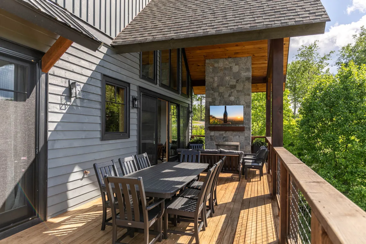 An inviting outdoor dining area featuring a large dining table, a stone fireplace, and lush greenery. The space is designed for groups to enjoy alfresco meals, celebrations, or relaxed evenings by the fire, all with the backdrop of a scenic view.