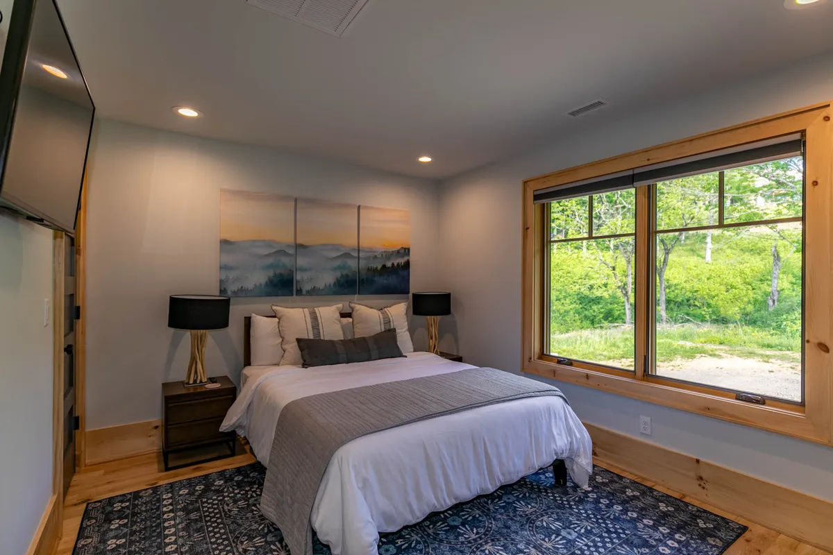 A tranquil bedroom with a large bed, window offering natural light and scenic views, tasteful artwork above the headboard, and matching nightstands. The room exudes a serene, calming atmosphere ideal for restful sleep or peaceful reading.